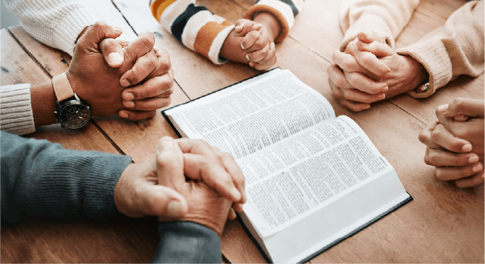 Open Bible with five sets of folded hands - picture